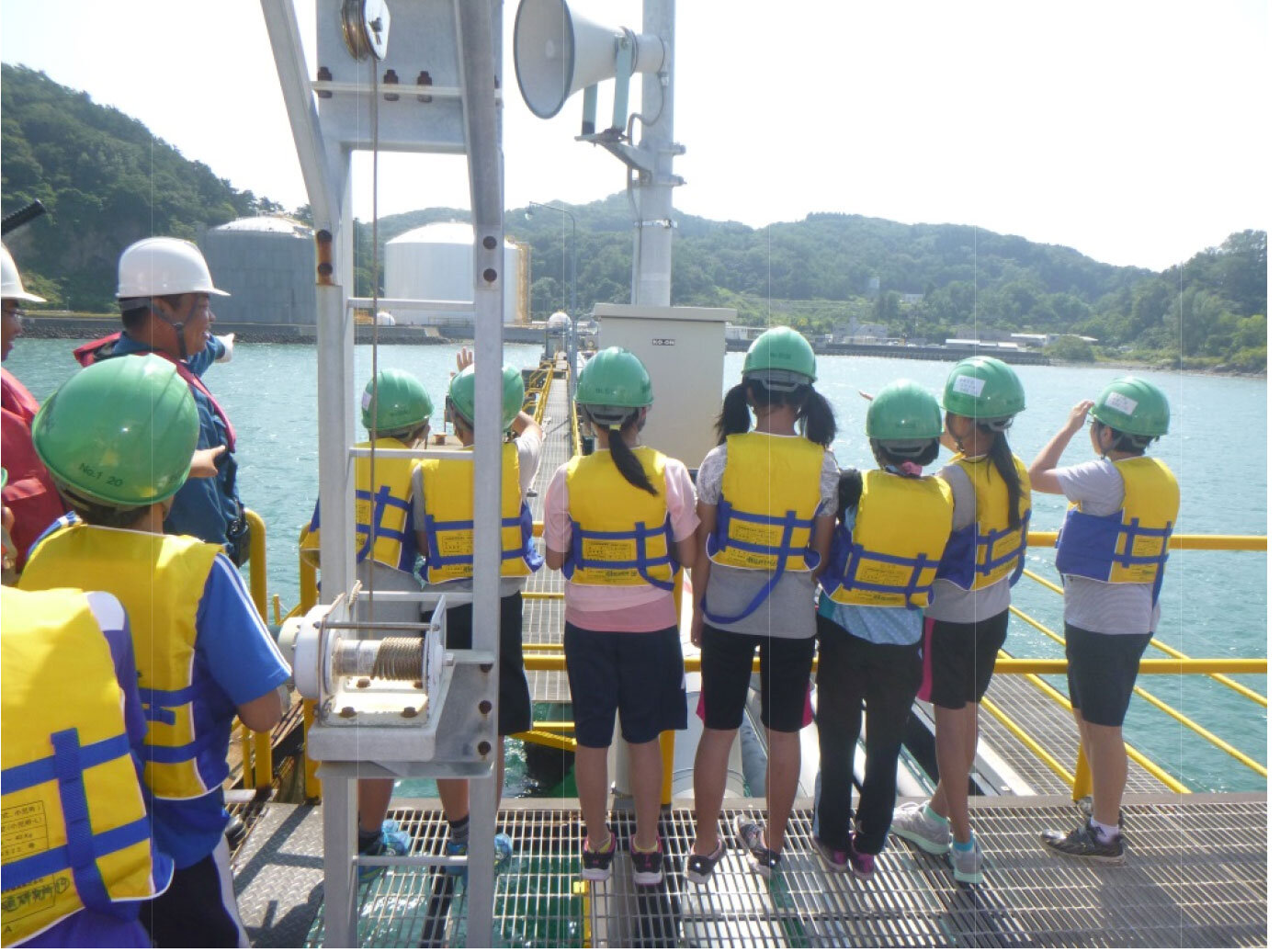 大型船桟橋から輸入タンクを見学しながら所員の説明を受ける生徒たち